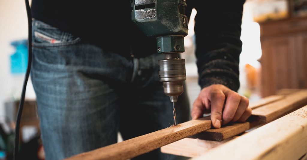 Close-up of a person using an electric drill on a wooden plank, showcasing detailed woodworking skills.
